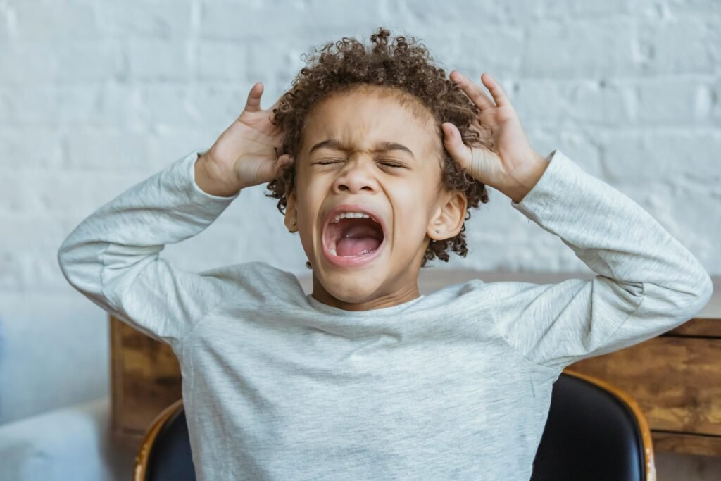 pexels-photo-6624327-6624327 Young boy showing frustration indoors with hands on head, eyes closed, mouth open.